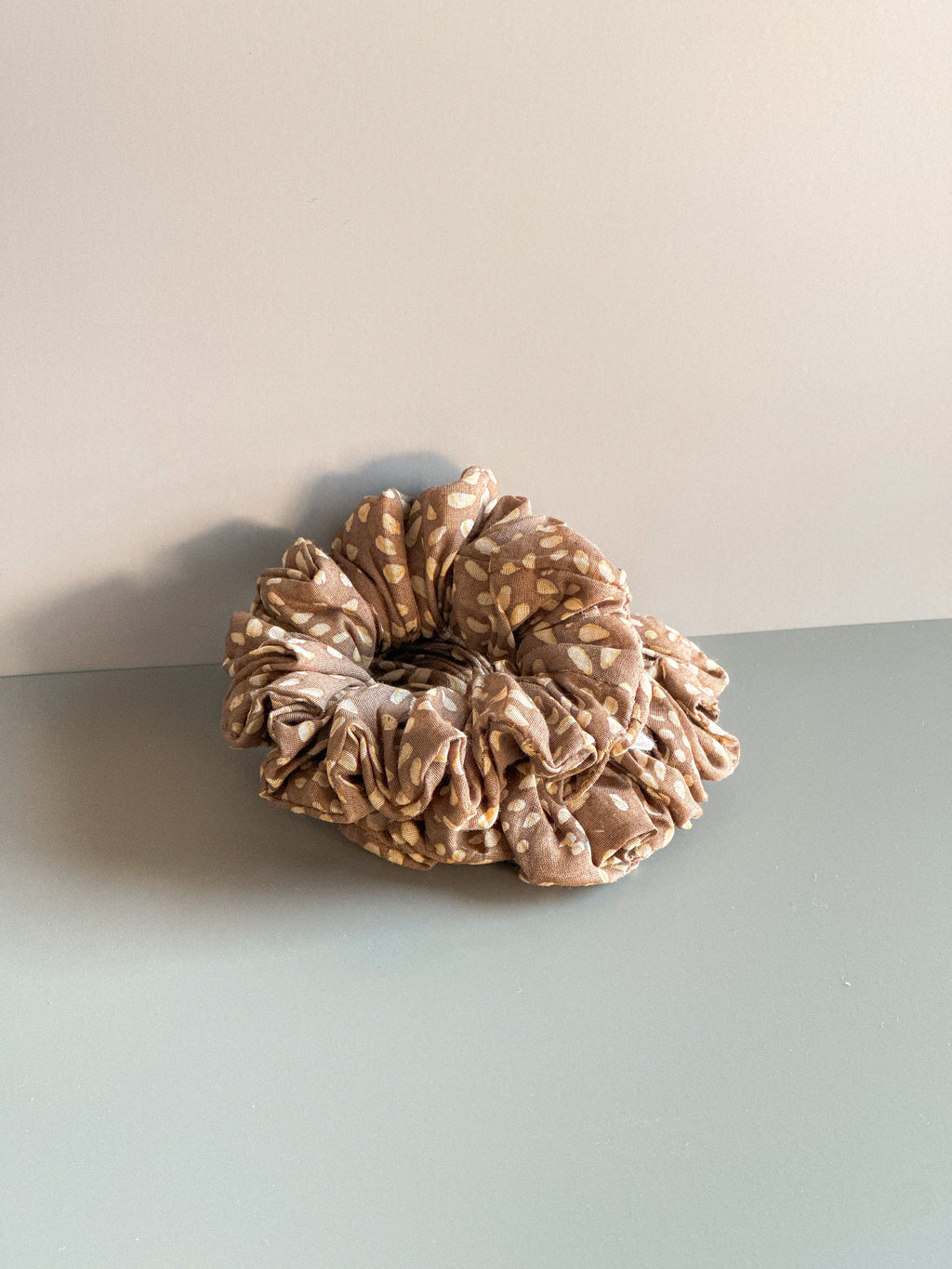 Brown scrunchie on a light gray surface with a beige background