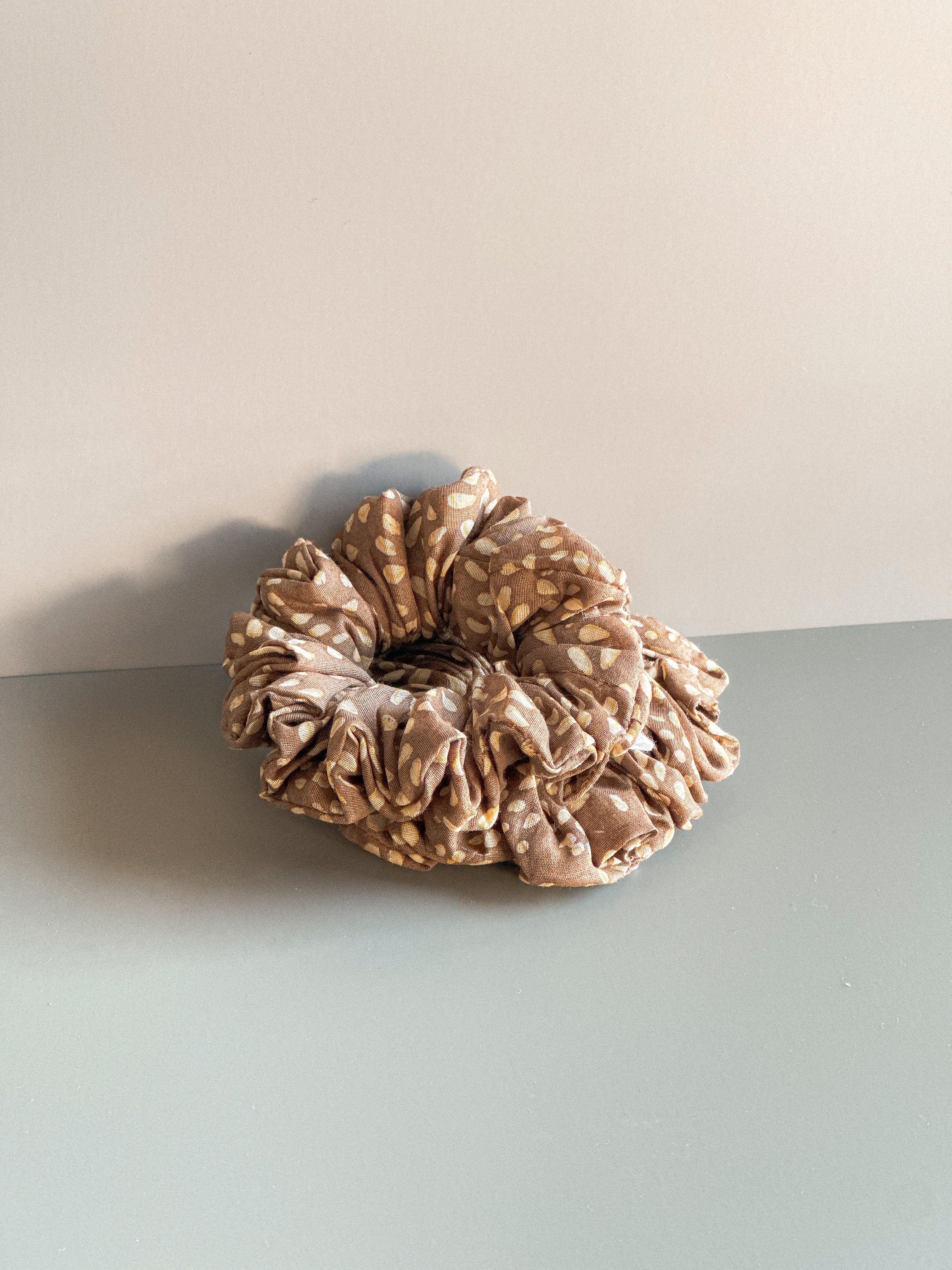 Brown scrunchie on a light gray surface with a beige background