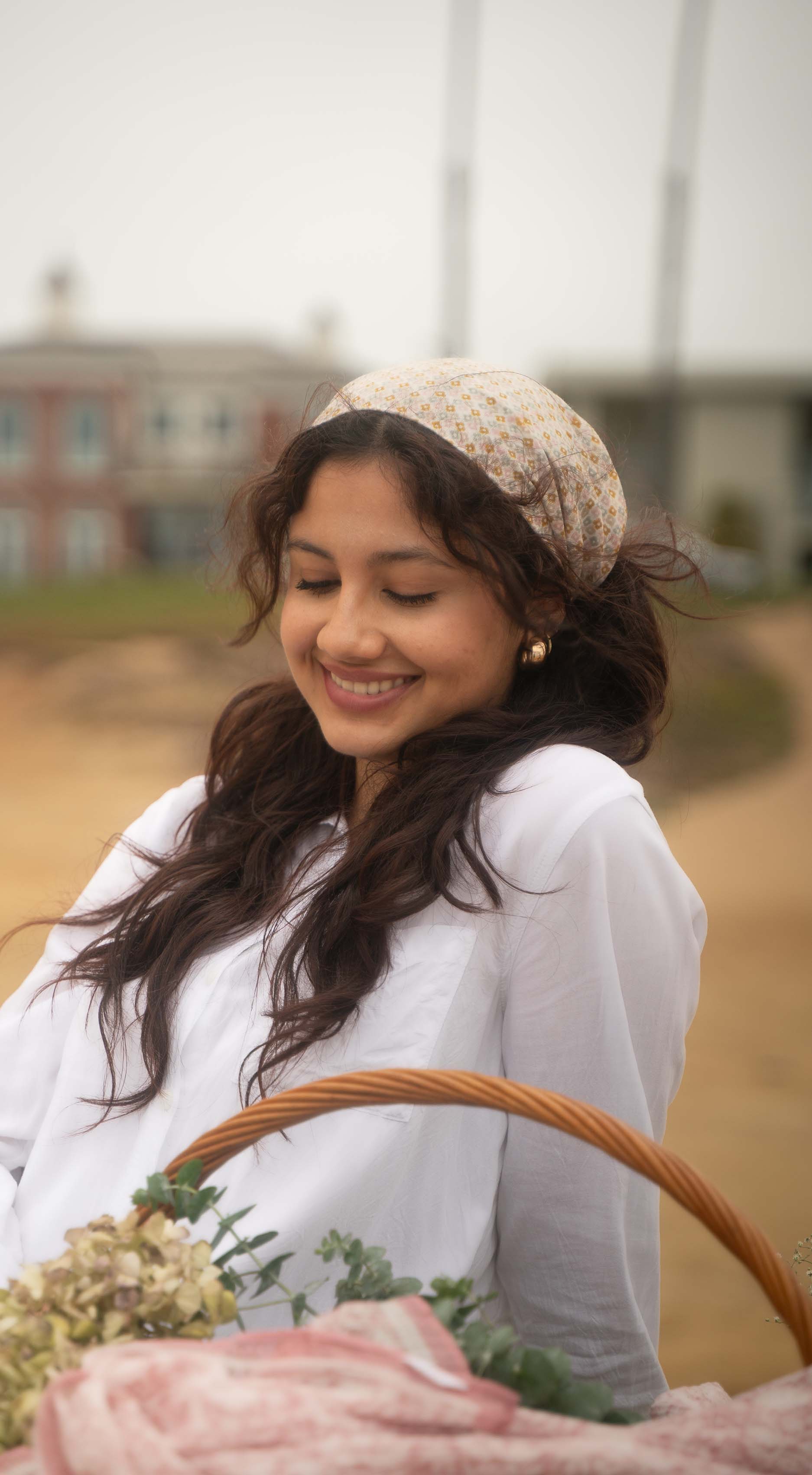 Woman in a white dress with a headscarf, holding a basket, outdoors.