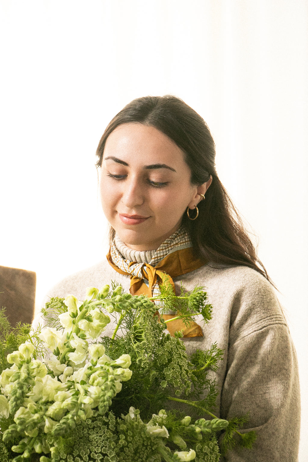 A woman wearing a block printed  neck scarf with a mustard yellow border, holding a bouquet of flowers.