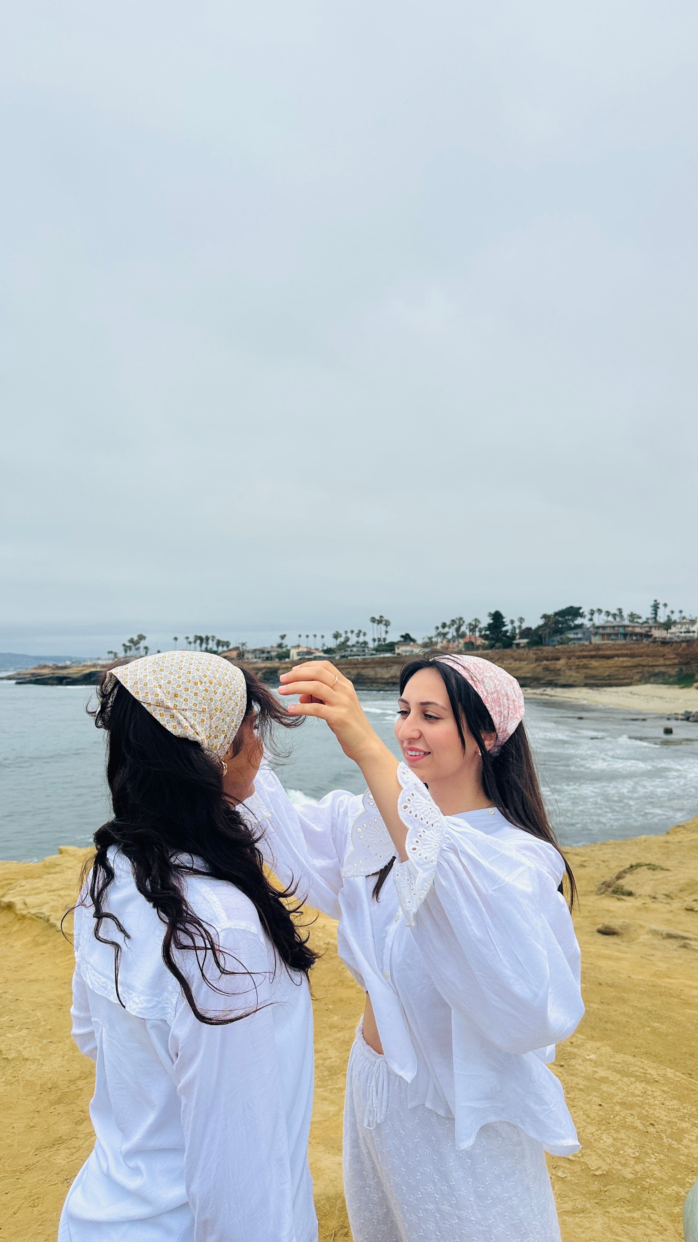 Two women in white outfits with block printed headscarves standing on a beach.