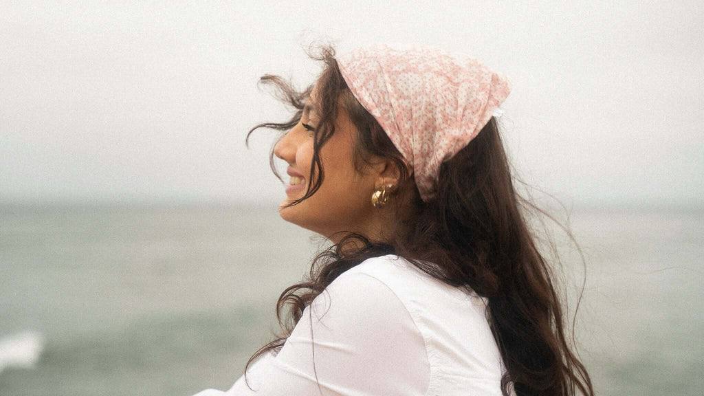 Woman with a pink headscarf sitting by the ocean