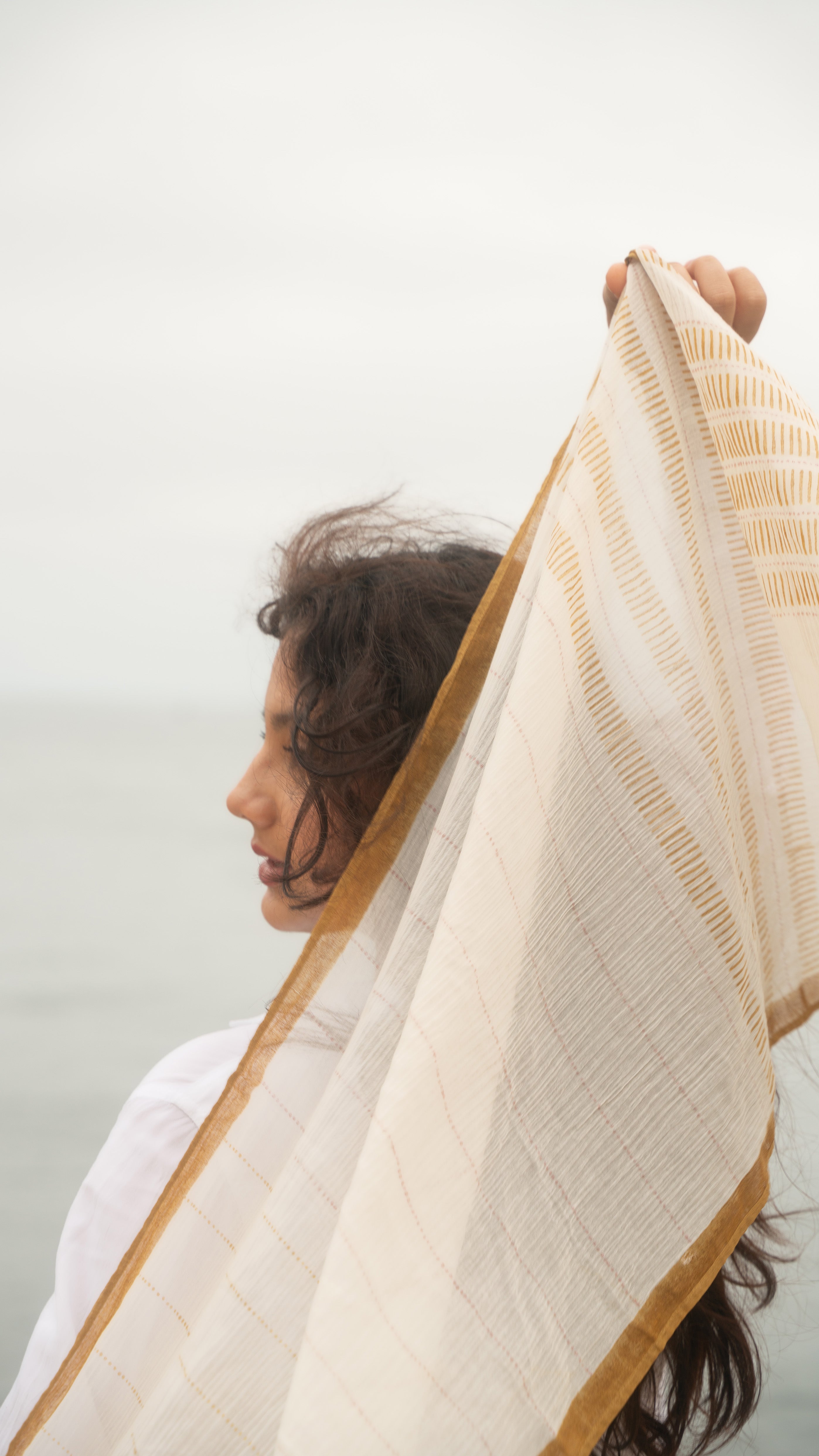 Woman holding a beige and white shawl against a light background