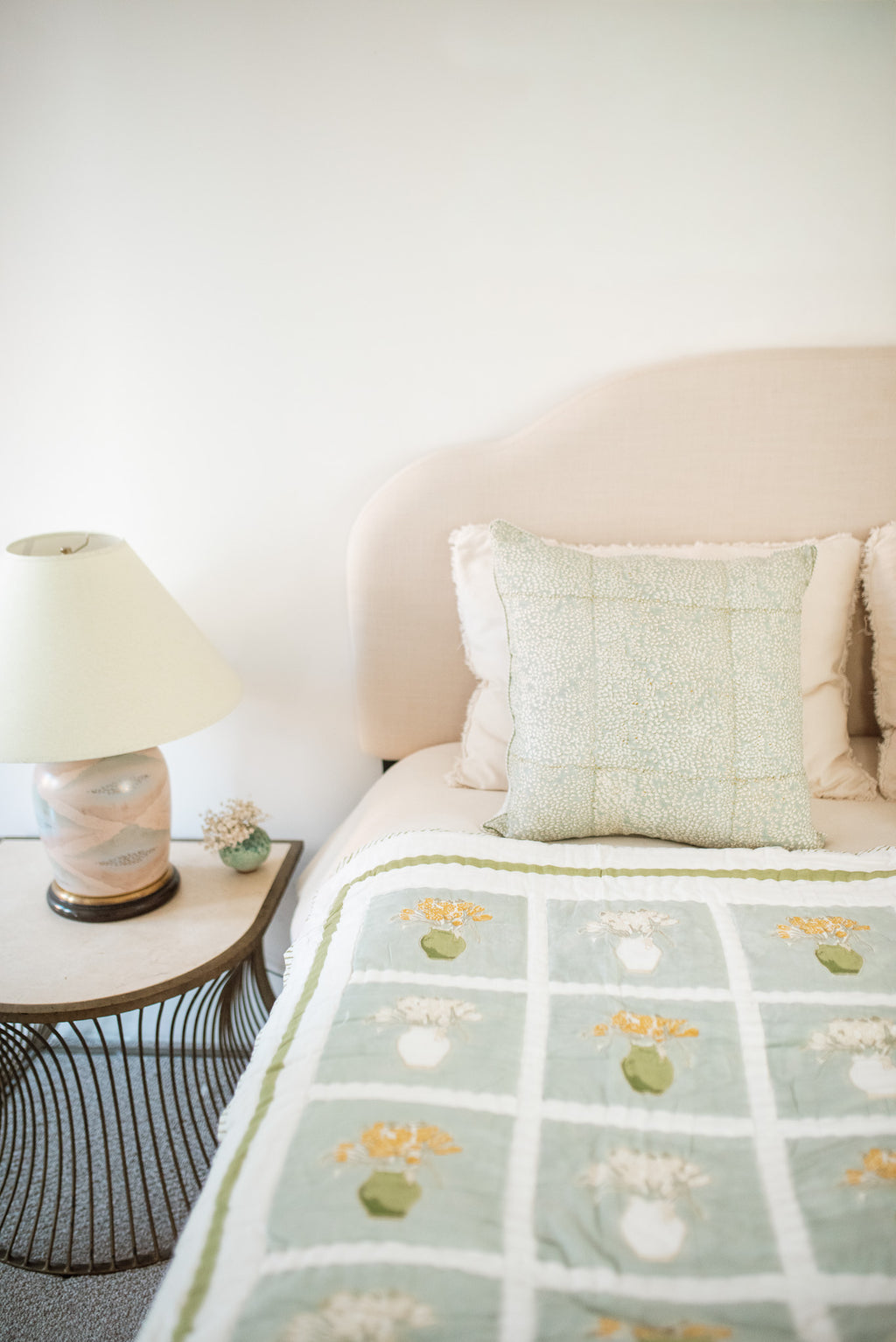Bedroom with a bed featuring a floral blanket, side table with lamp, and white wall.