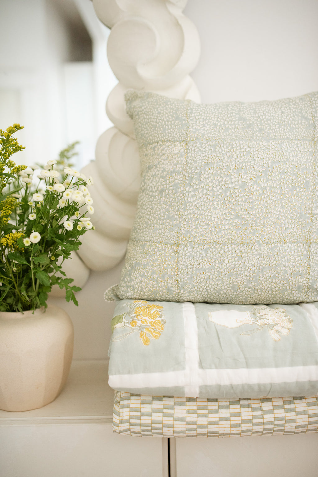 Decorative pillow and floral arrangement on a shelf with a textured wall in the background