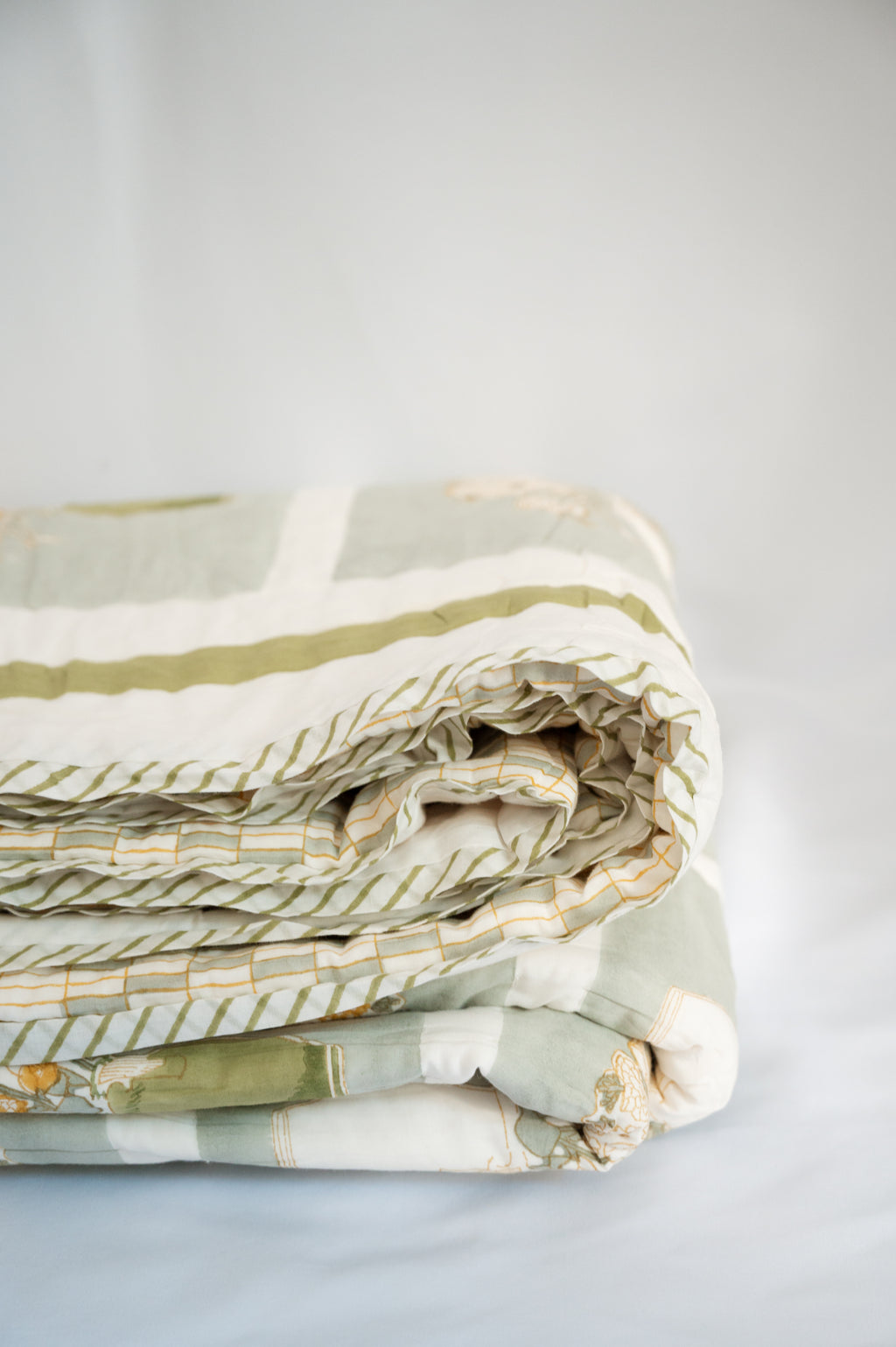 Folded fabric with green and beige patterns on a light gray background